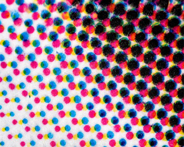 Magnified CMYK print dots showing cyan, magenta, yellow, and black halftone pattern on paper close-up.